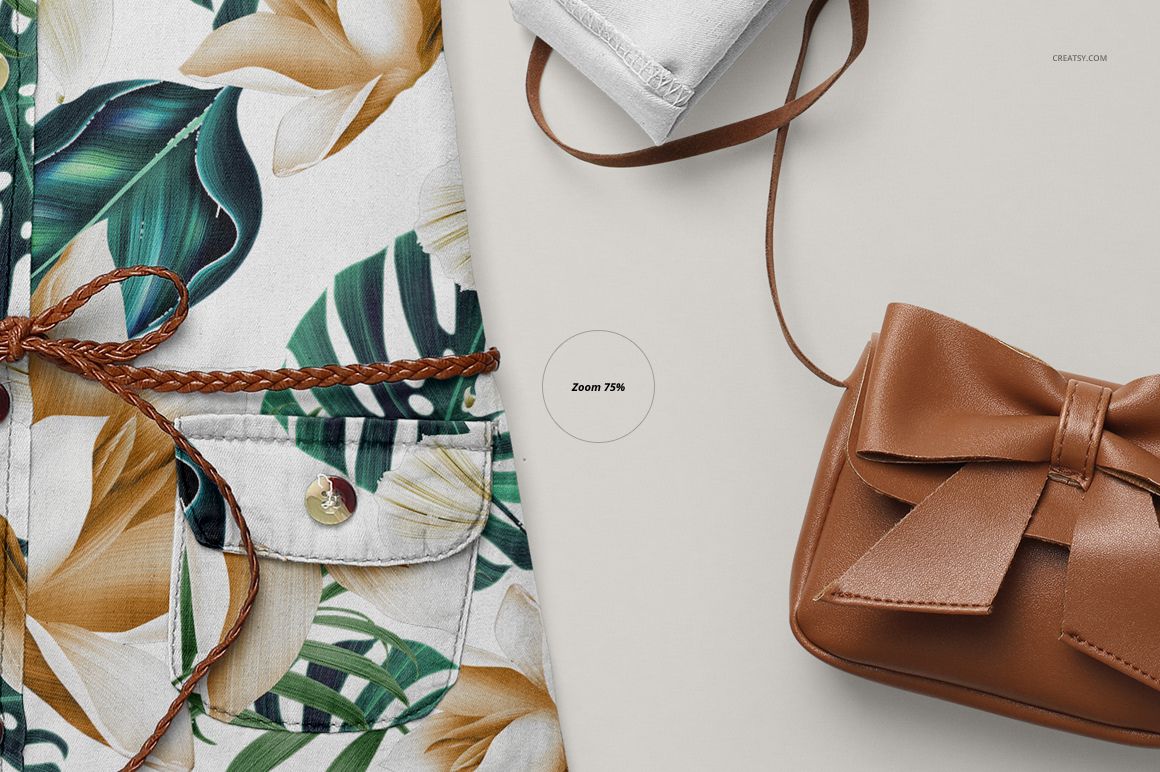 Close-up front view of a baby jeans dress mockup with tropical leaf and flower pattern, brown braided belt, and a brown purse.