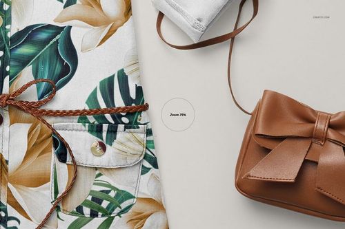 Close-up front view of a baby jeans dress mockup with tropical leaf and flower pattern, brown braided belt, and a brown purse.
