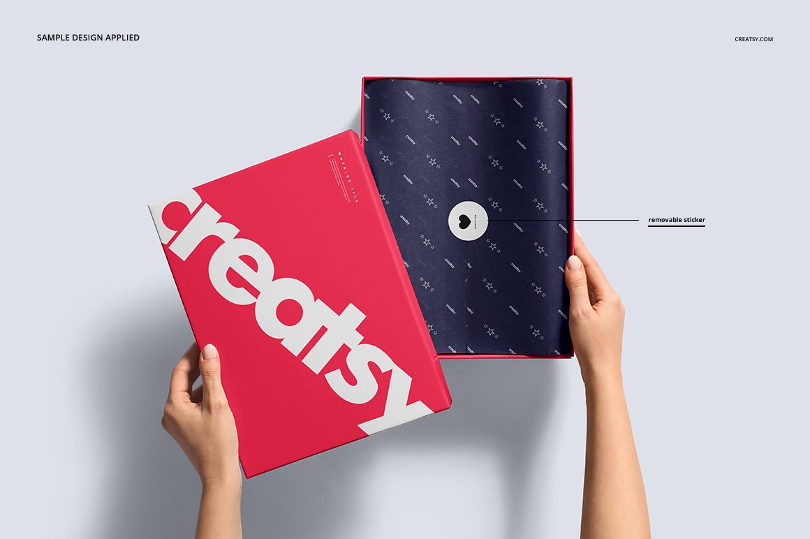 Hands holding an open rectangular shoe box mockup with a bold pink lid and patterned navy interior on a light background.