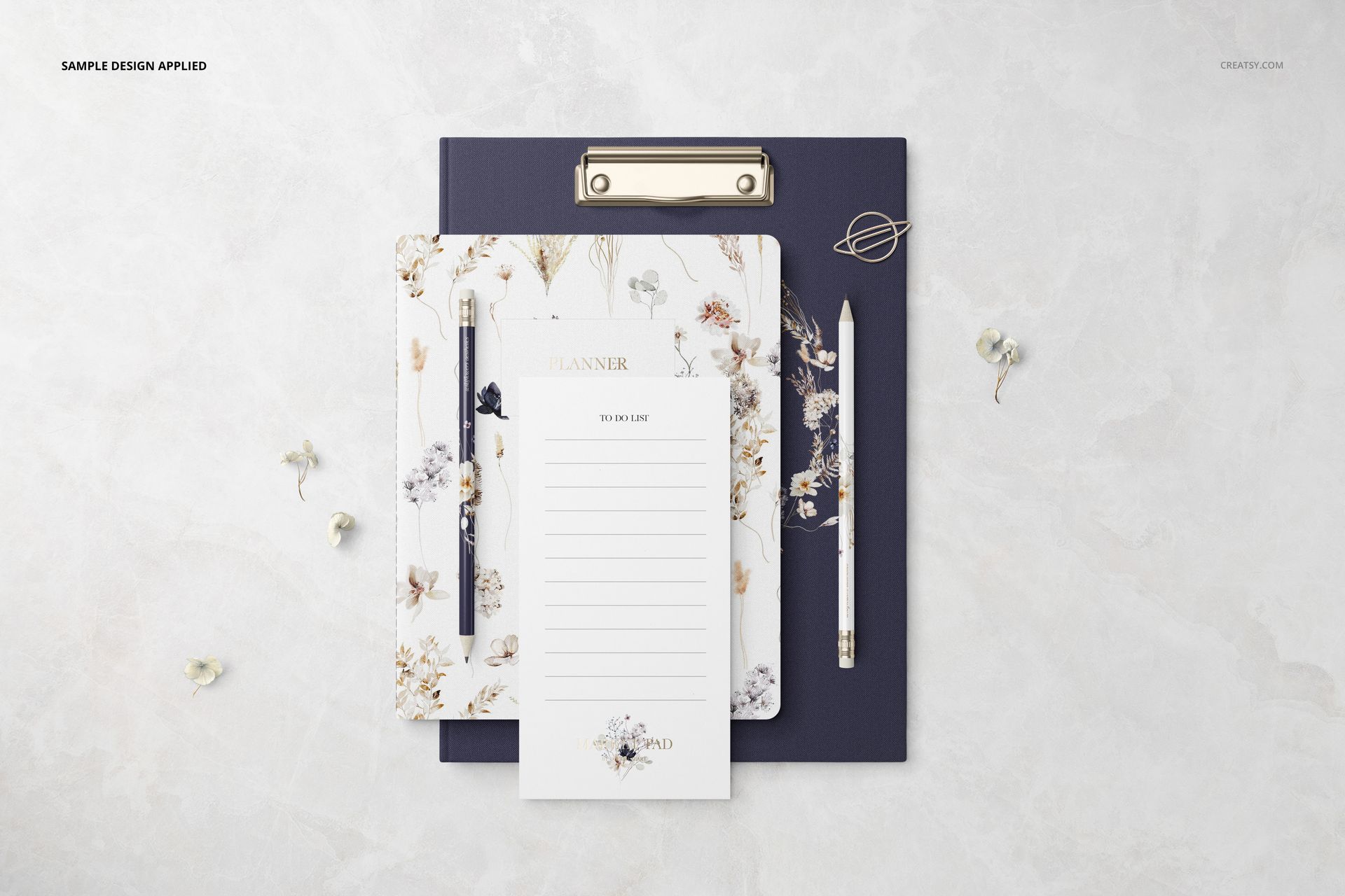 Top view of a stationery set mockup with a floral planner, notepad, dark clipboard, pen, and decorative clips.