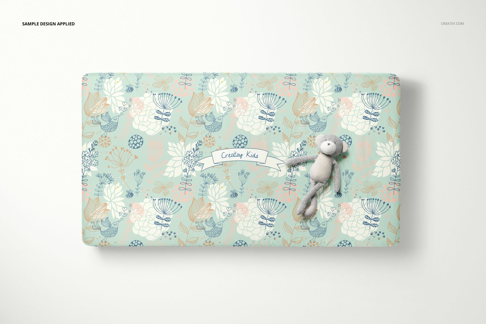 PSD mockup showing a rectangular crib sheet with soft blue and beige botanical designs, toy placed on the sheet.