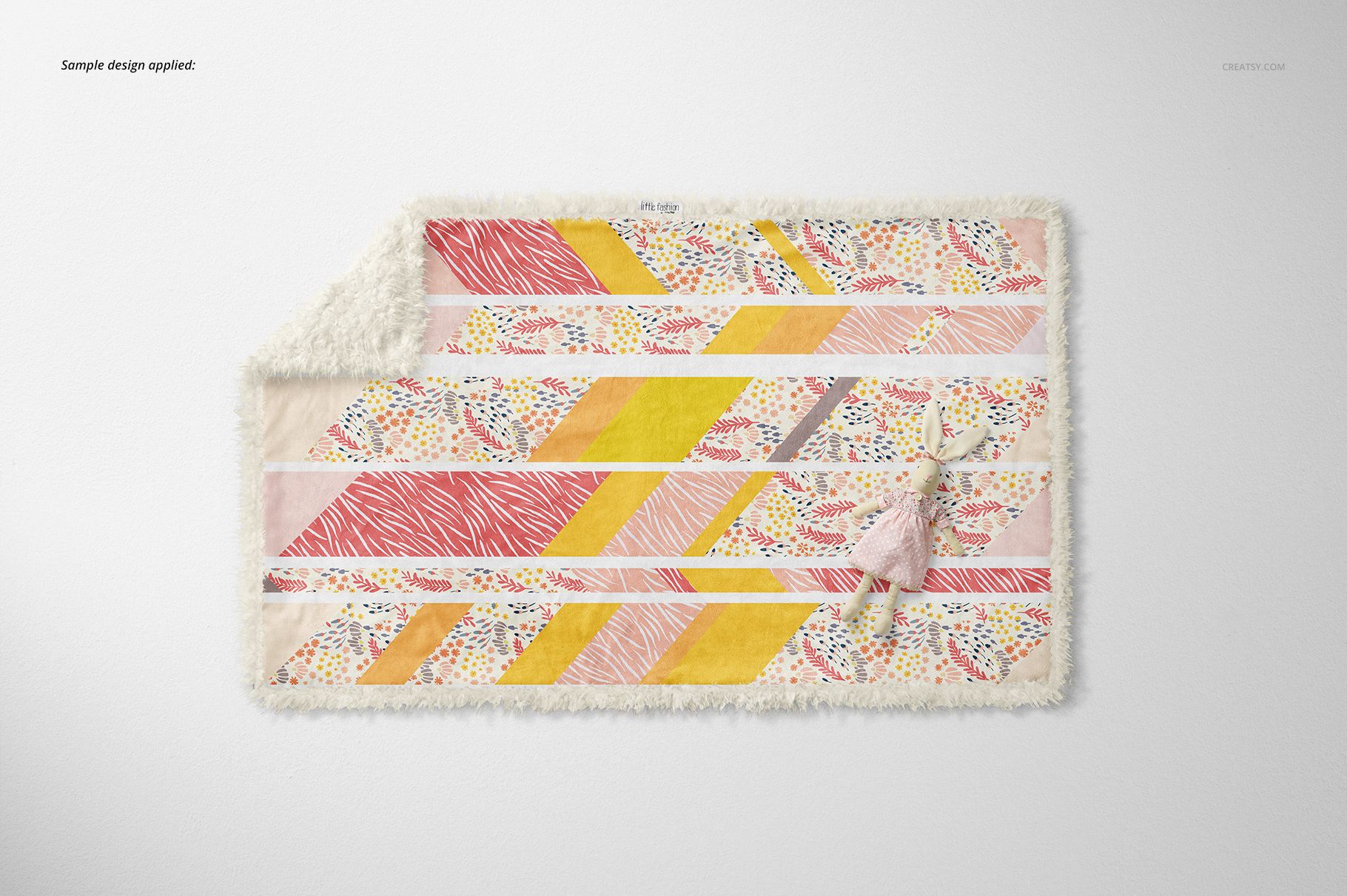 Top view of a sherpa baby blanket mockup featuring yellow, pink, and multicolored stripes, with a soft toy beside it.