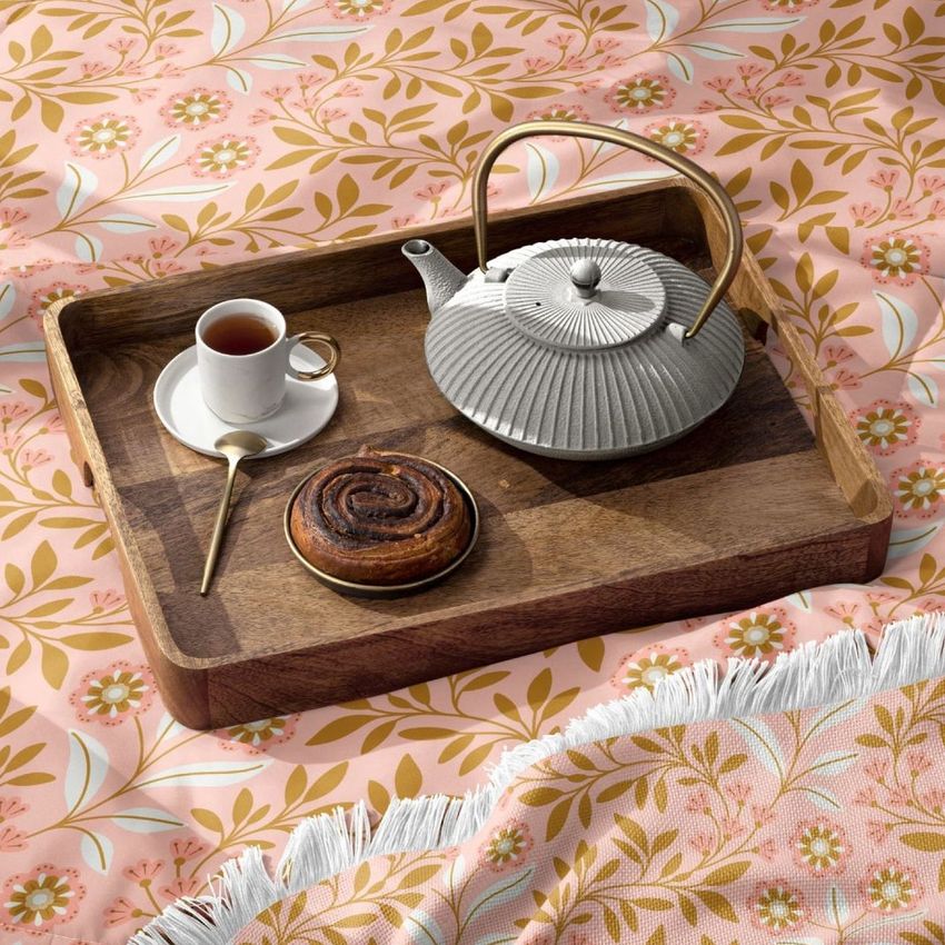 Microfiber comforter mockup featuring a pink and gold floral pattern, with a wooden tray holding a teapot, cup of tea, and pastry.