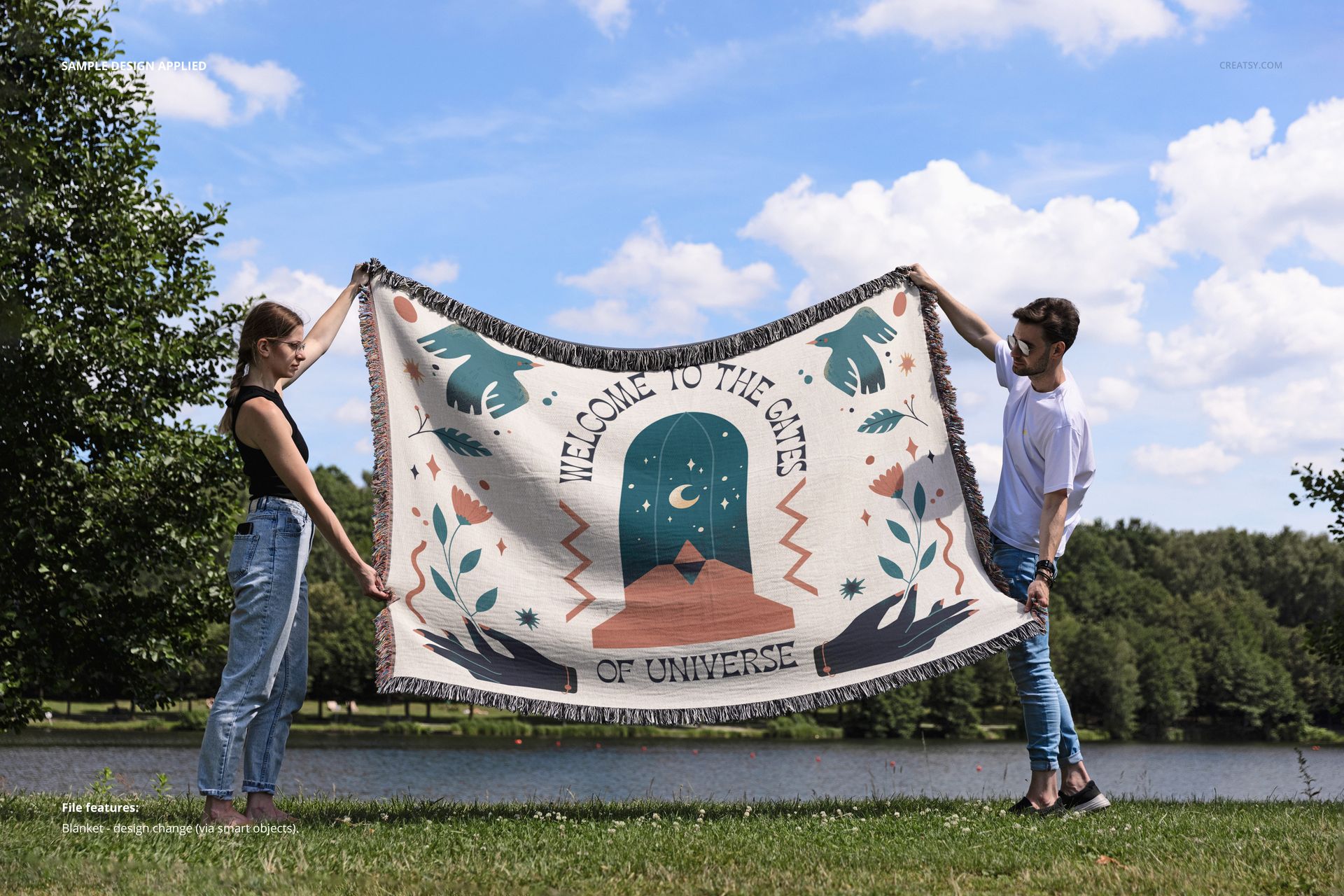 Front view of a fringed woven throw blanket mockup held by two people near a lake, featuring a bold pattern.