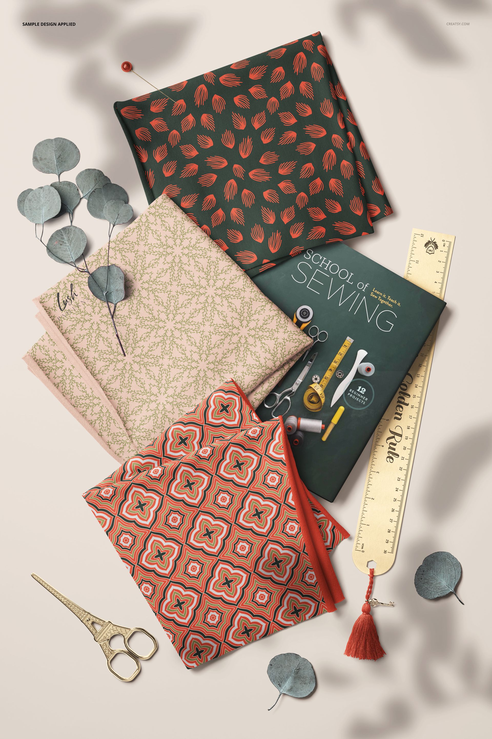 Top view of three patterned jersey fabric pieces in red, pink, and black, arranged beside a sewing book and ruler mockup.