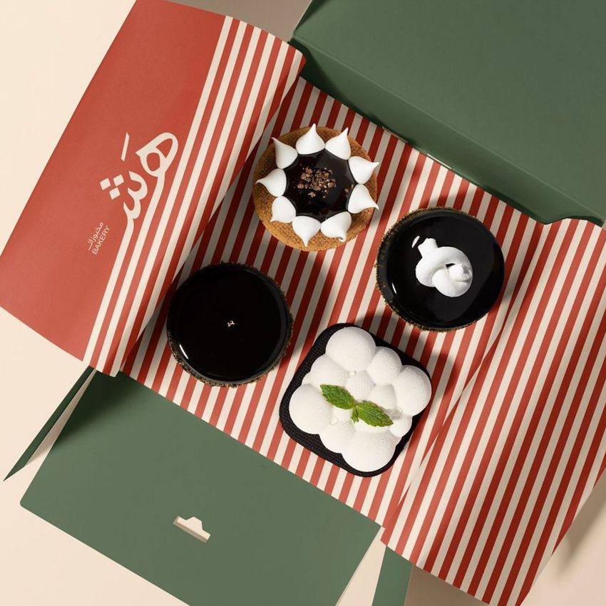 Food safe paper mockup with red and white stripes lines the inside of a green box holding assorted desserts viewed from above.