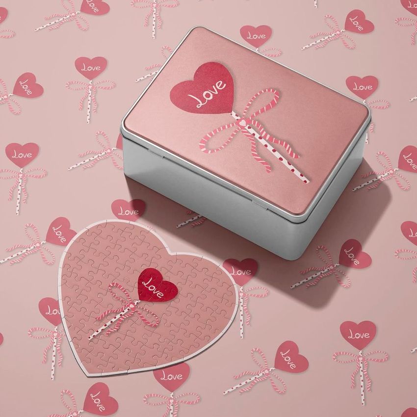 Heart-shaped jigsaw puzzle mockup and horizontal puzzle box on a pink surface with repeating lollipop and heart patterns.
