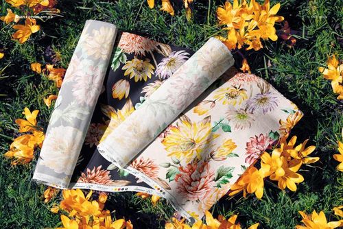 PSD mockup of floral fabric rolls arranged on grassy ground, accented by scattered yellow blossoms in sunlight.