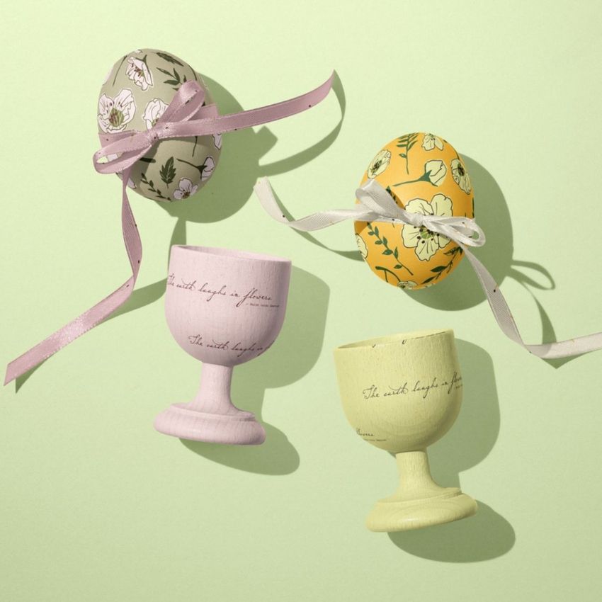 Easter egg crafts mockup showing two decorated eggs with floral patterns and ribbons, placed above pastel egg cups on a light green background.