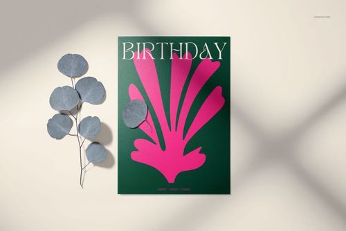Front view of a 5x7 greeting card mockup with a green cover, pink abstract design, and birthday text, beside dried leaves.