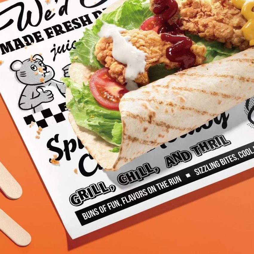 Food safe paper mockup featuring a tortilla wrap filled with fried chicken, lettuce, tomato, and sauces on a bright orange surface.