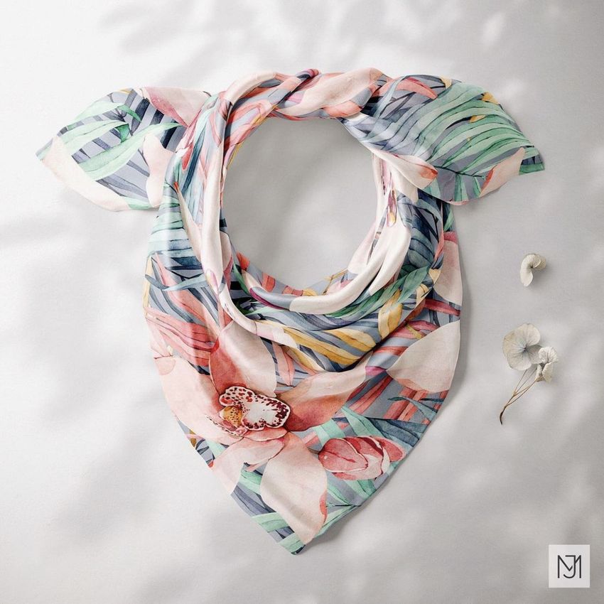 Silk scarf mockup with a tropical floral pattern in pastel shades, arranged in a circle on a light surface with dried flowers nearby.