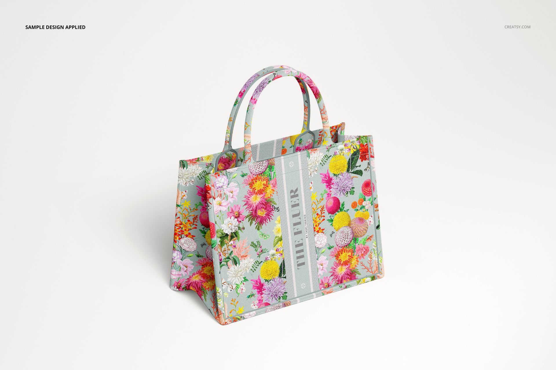 PSD mockup of a canvas tote bag featuring bright multicolored flowers, shown in three-quarter view on white surface.