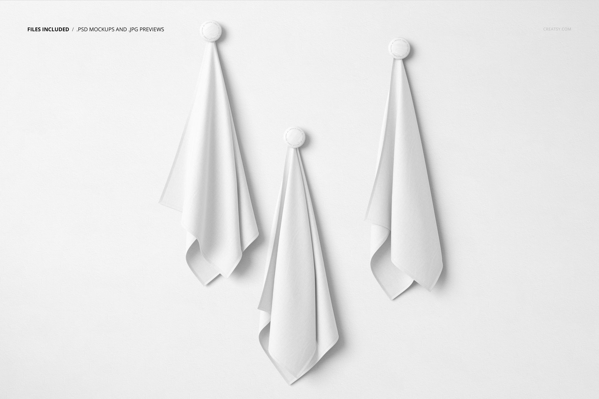 PSD mockup featuring trio of white textiles hanging vertically from knobs on a smooth, neutral wall surface.