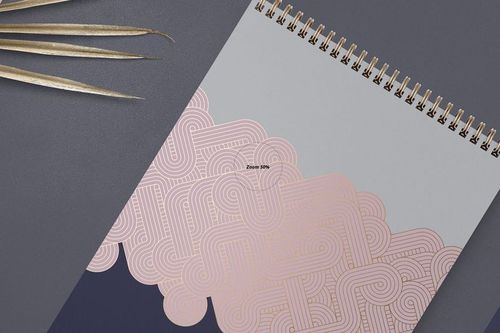 A4 vertical spiral notebook mockup with gold spiral binding, featuring geometric pink and gray patterns, top view.