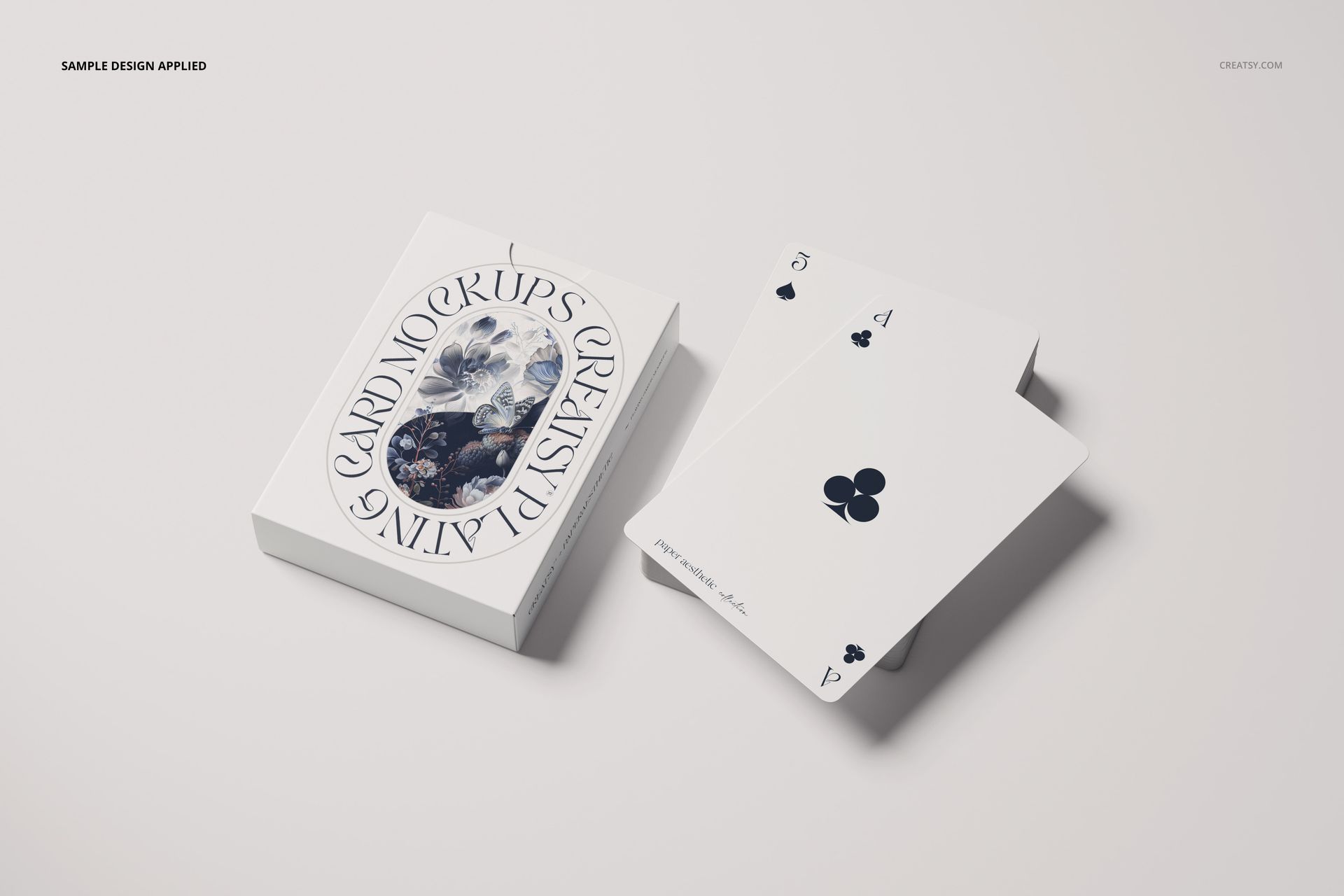 Playing cards mockup featuring a white card box with artistic design and two club cards, shown on a light surface.