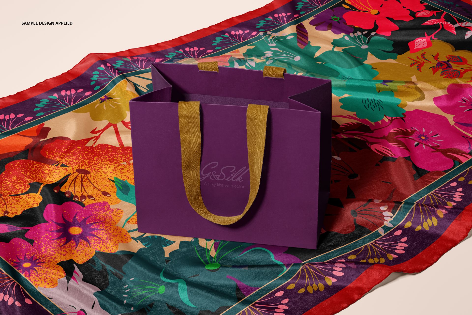Front view of a purple paper bag with gold handles placed on a colorful floral habotai silk scarf mockup.
