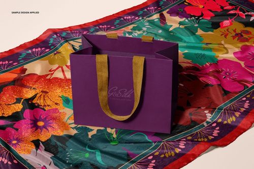 Front view of a purple paper bag with gold handles placed on a colorful floral habotai silk scarf mockup.