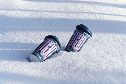 Winter-themed PSD mockup featuring two drinkware paper cups with black lids resting in deep snow, angled perspective.