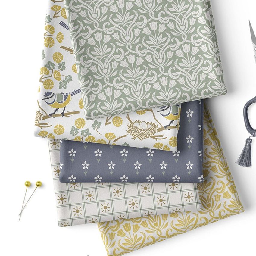 Folded fabrics mockup featuring four patterned textile pieces in muted green, yellow, and blue tones, arranged on a white surface.
