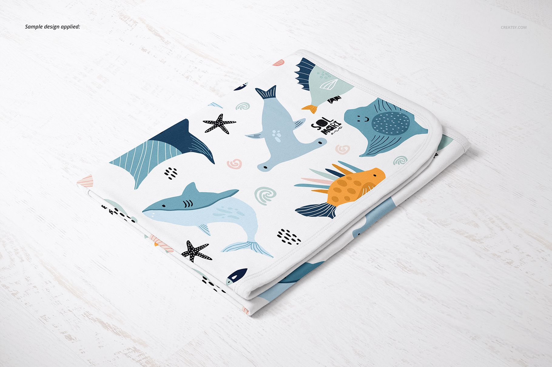 Cotton baby blanket mockup featuring playful aquatic animal patterns, displayed folded on a light wooden background.