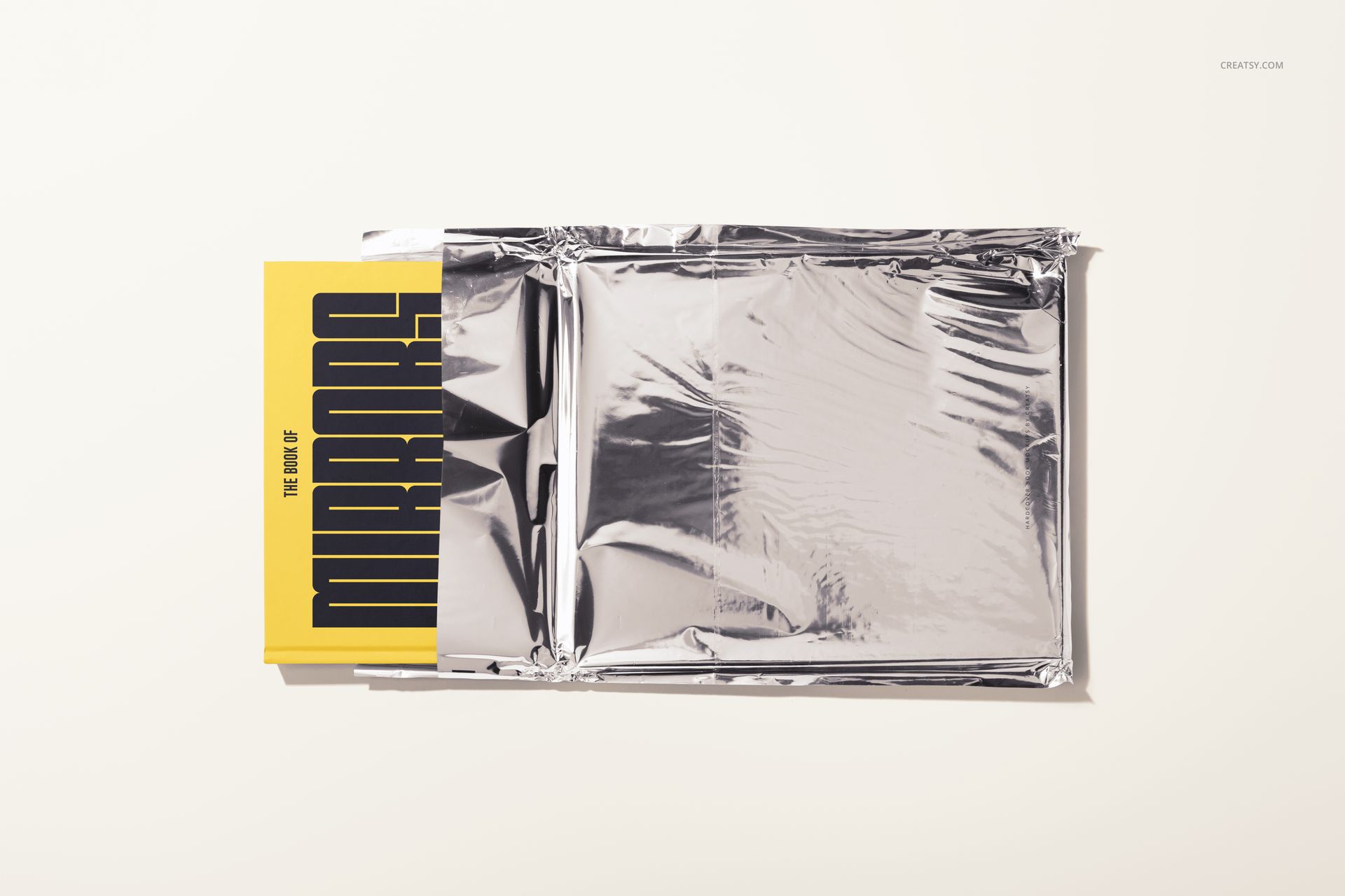 Top view of a hardcover book mockup featuring a yellow cover with black lettering, partially covered by metallic foil.