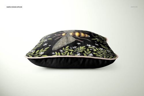 Mockup of a rectangular silk cushion with braided trim, black background, and floral bee artwork, side perspective.