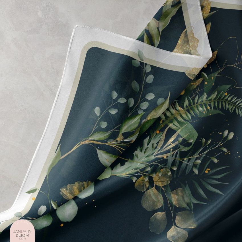 Closeup of a silk scarf mockup featuring a botanical foliage pattern in green and gold on a dark background, draped on a light surface.