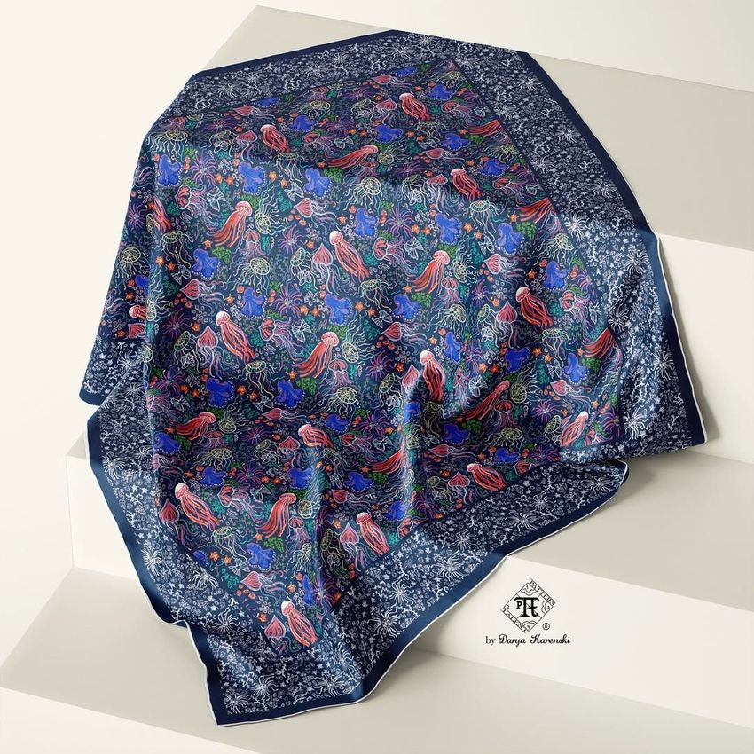 Silk scarf mockup draped over light-colored stairs, featuring a vibrant neon sea life pattern with fish and coral on a dark background.