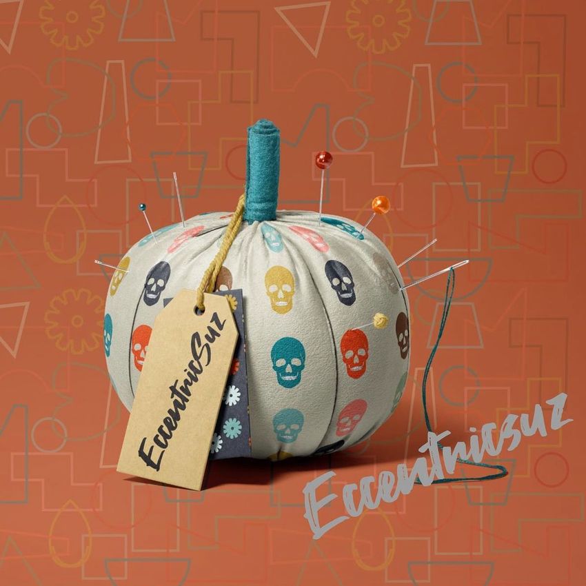 Fabric pumpkin mockup with colorful skull pattern, used as a pincushion with pins and a tag, on an orange geometric background.