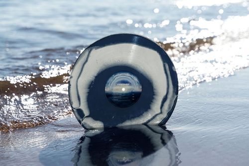 Mockup of a marbled vinyl record in shades of gray and black positioned on sandy beach by gentle waves.