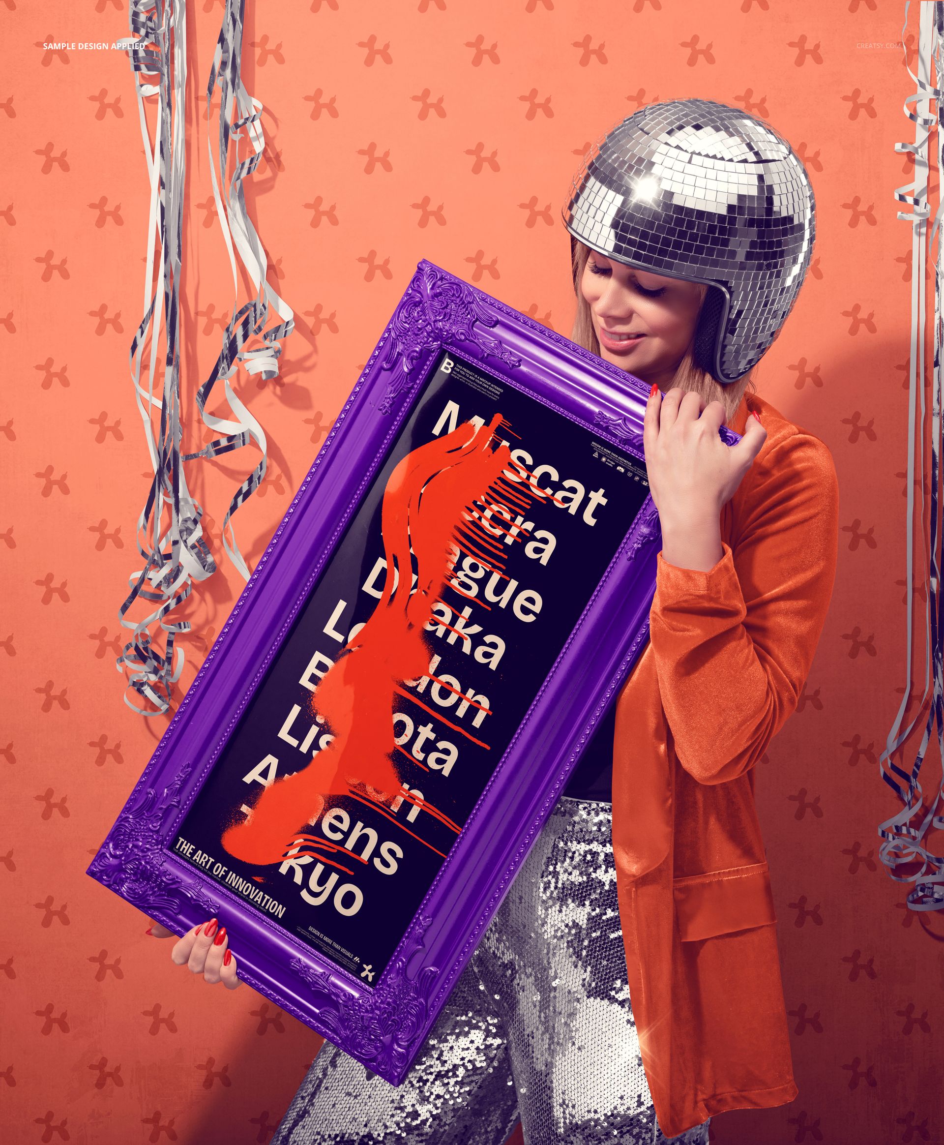Framed art print mockup in purple frame held by model, orange wall with festive silver streamers in background.