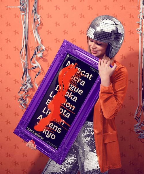 Framed art print mockup in purple frame held by model, orange wall with festive silver streamers in background.