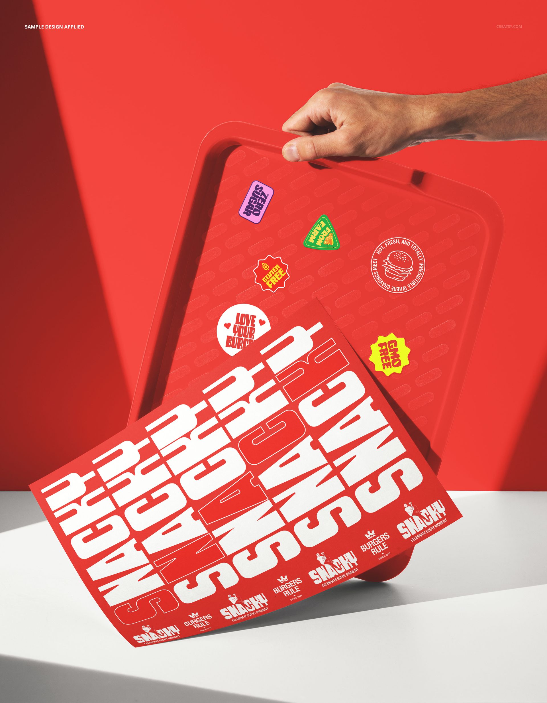 Hand holding a red fast food tray decorated with stickers and large white letters, presented in a PSD mockup scene.