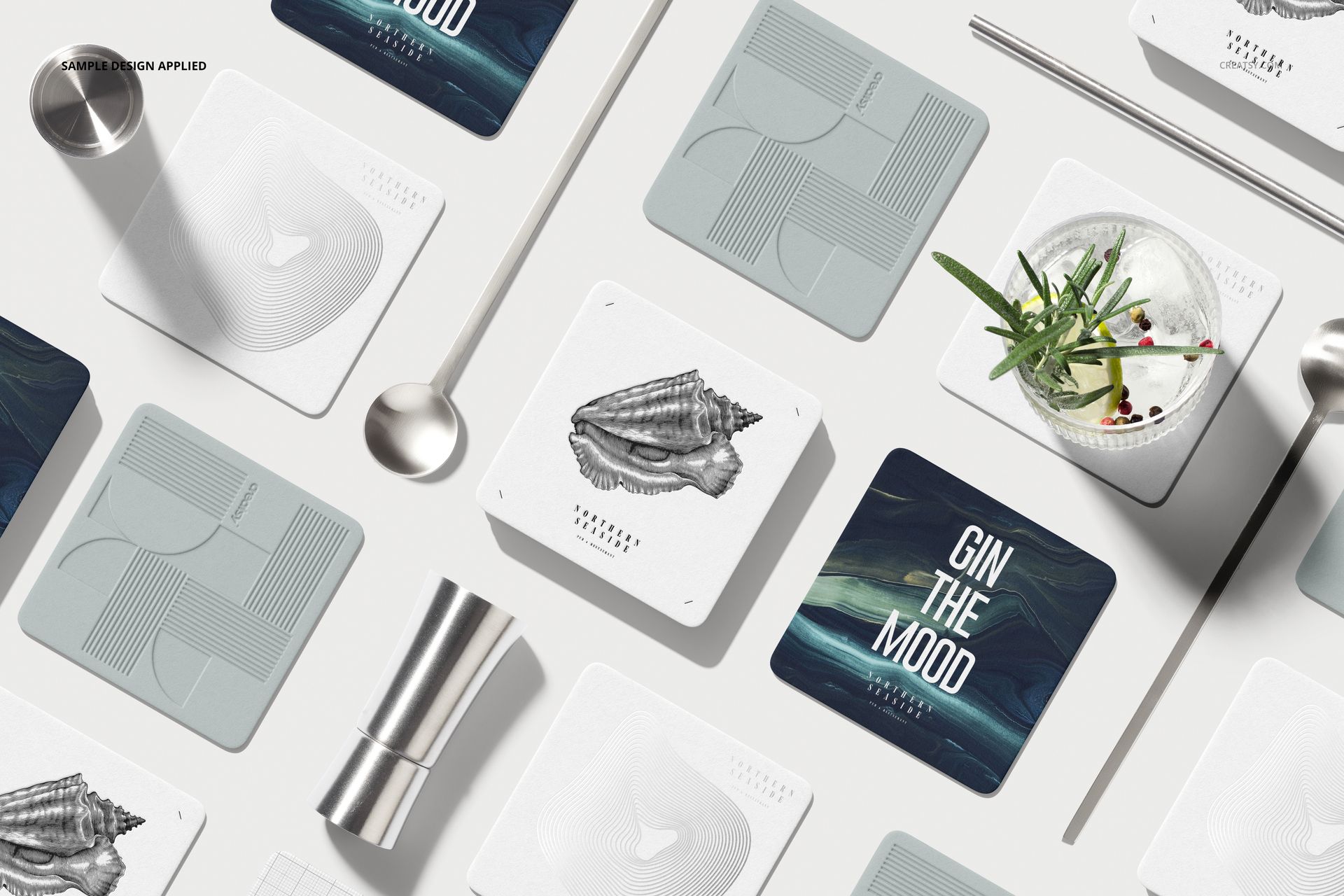 Mockup set showing square coasters in different designs, displayed on a white background with metal bar tools and a drink.