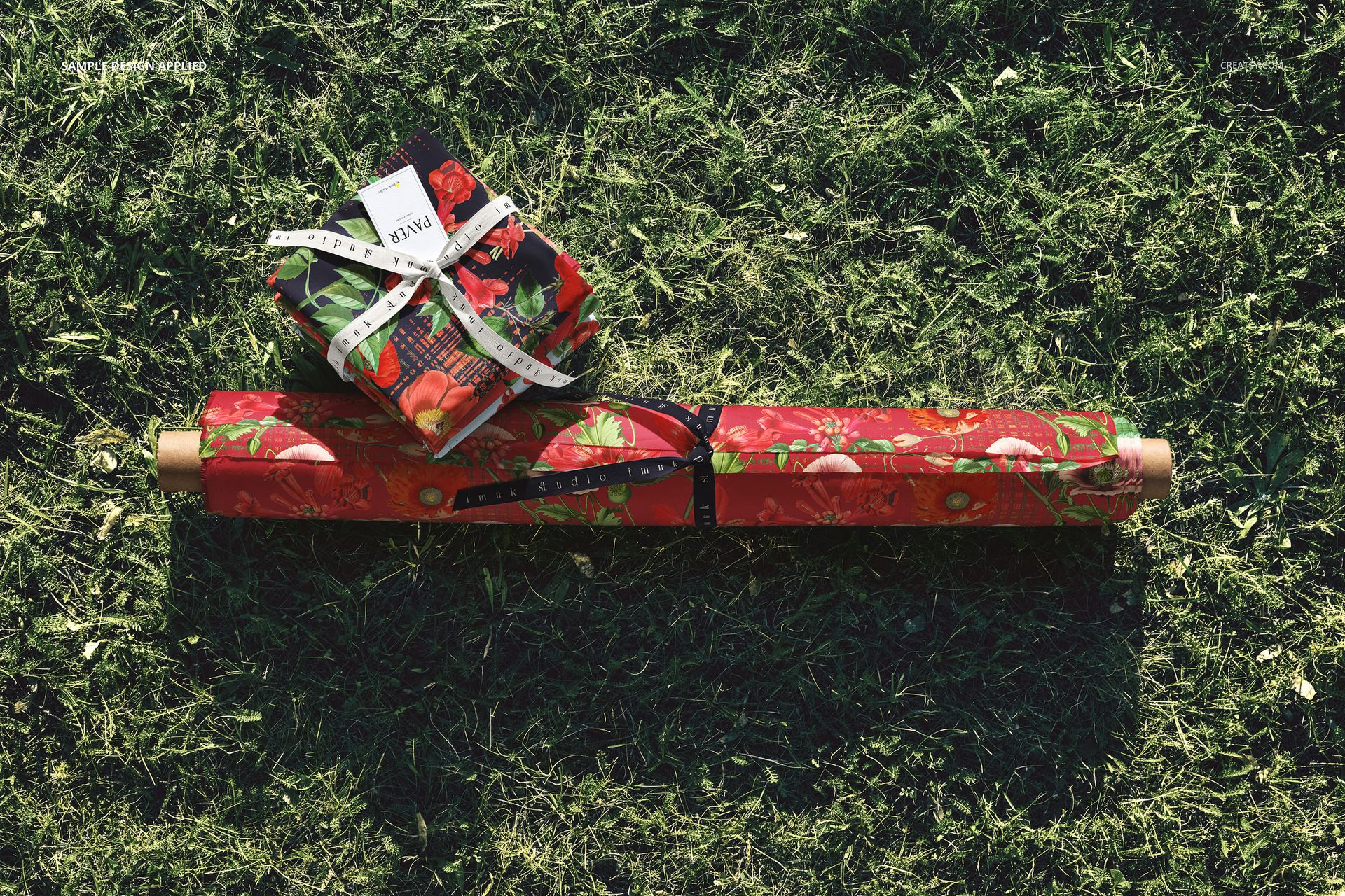 Fabric rolls and stacked fabric pieces with red fruit pattern lying on green grass, viewed from above.