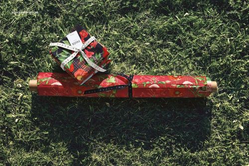 Fabric rolls and stacked fabric pieces with red fruit pattern lying on green grass, viewed from above.