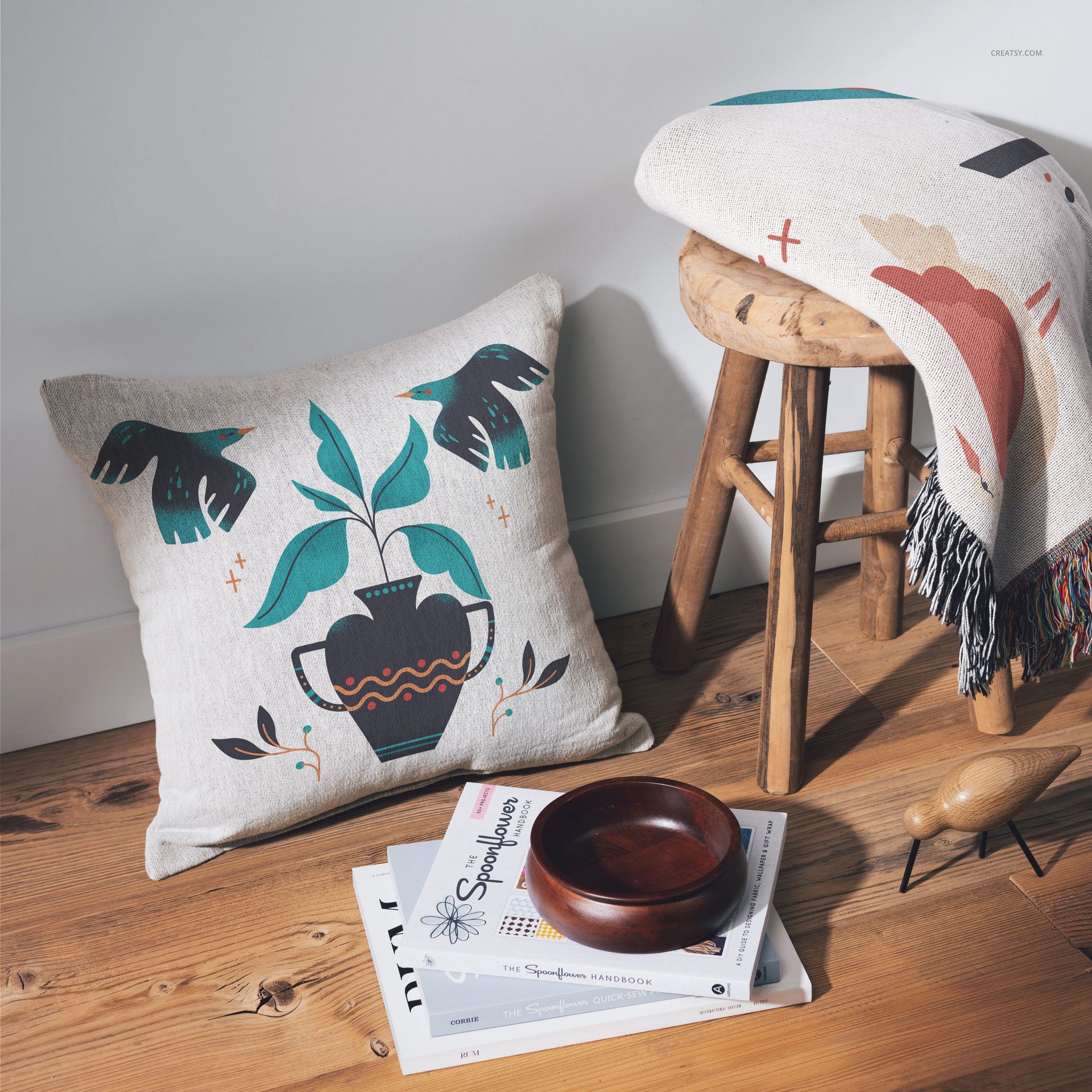 PSD mockup of a square pillow with leaf and vase artwork, placed on wood flooring with cozy home decor props.
