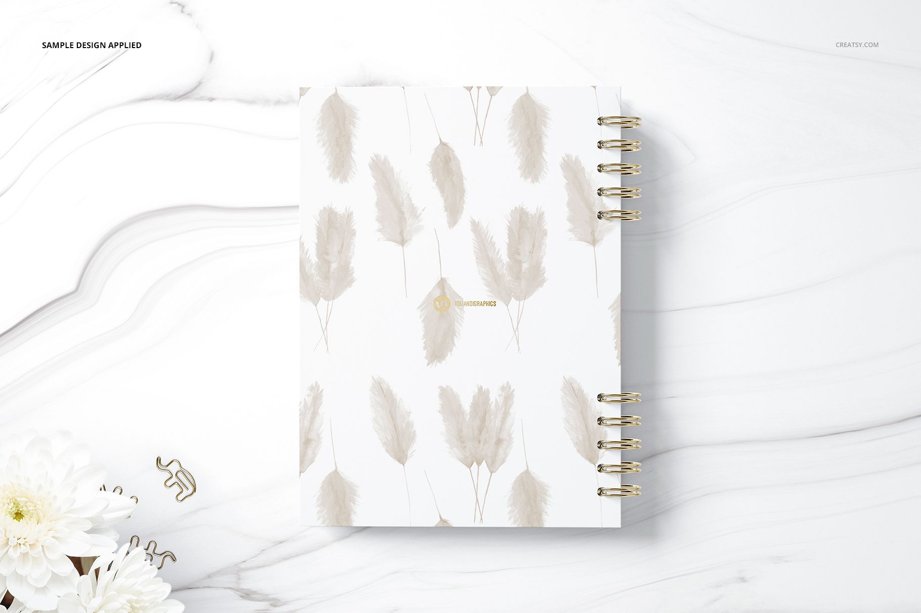 Spiral-bound planner mockup with a soft beige feather design on the front cover, placed on a white marble background.