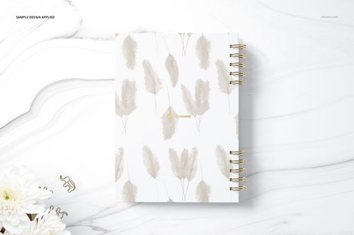 Spiral-bound planner mockup with a soft beige feather design on the front cover, placed on a white marble background.