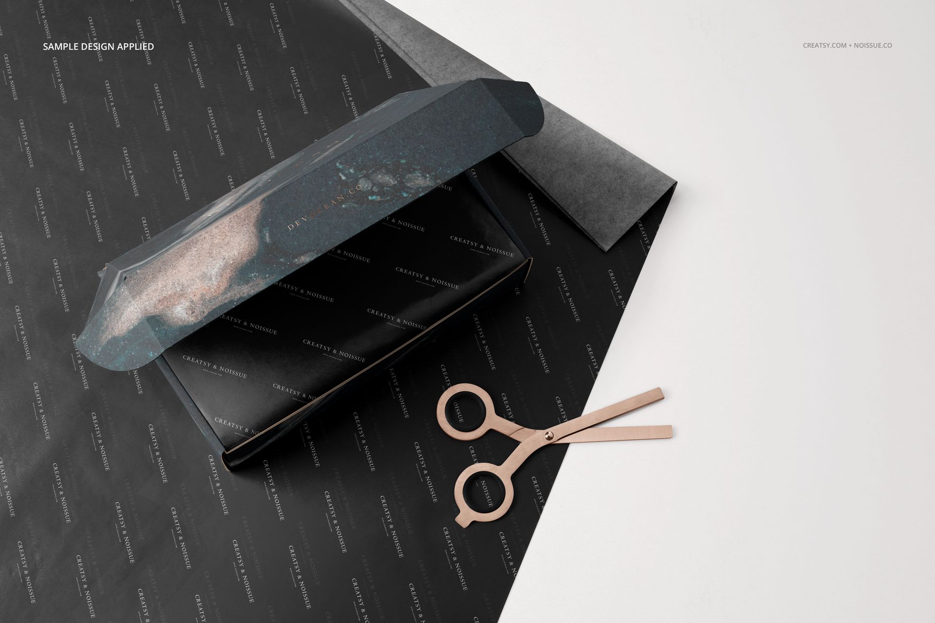 Rectangular mailing box mockup with dark patterned tissue paper, scissors, and a sheet of black wrapping paper, top view.