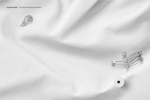 Wrinkled white fabric mockup with soft folds, viewed from above, featuring a button and safety pins on the surface.