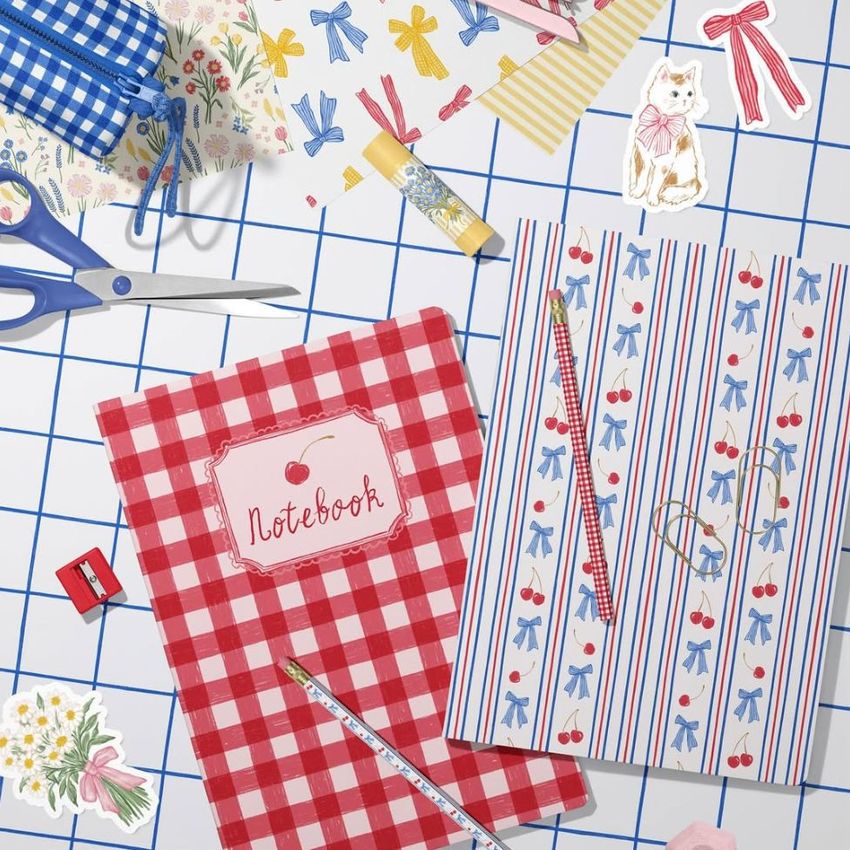 Stationery mockup featuring two A4 notebooks with cherry and bow patterns on a grid surface, surrounded by scissors, pencils, and decorative paper.