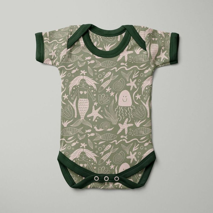 Baby short sleeve bodysuit mockup featuring a green and beige mermaid pattern with sea creatures on a flat background.