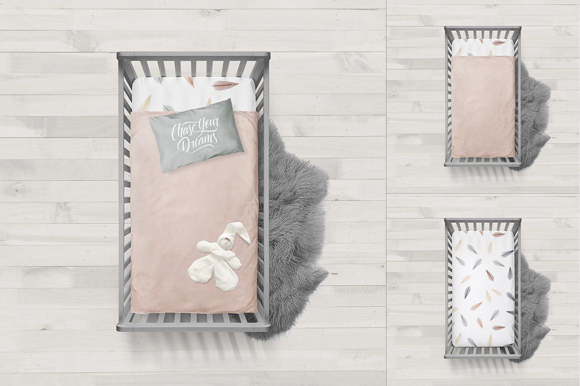 Top view of a crib bedding mockup with a gray crib, blush pink quilt, white pillow, and plush toys on a light wood floor.