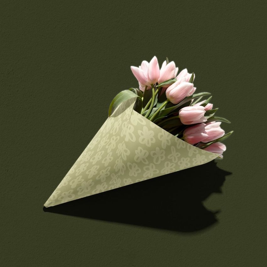 Flower packaging mockup showing a bouquet of pink tulips wrapped in light green paper with a floral pattern on a dark green surface.