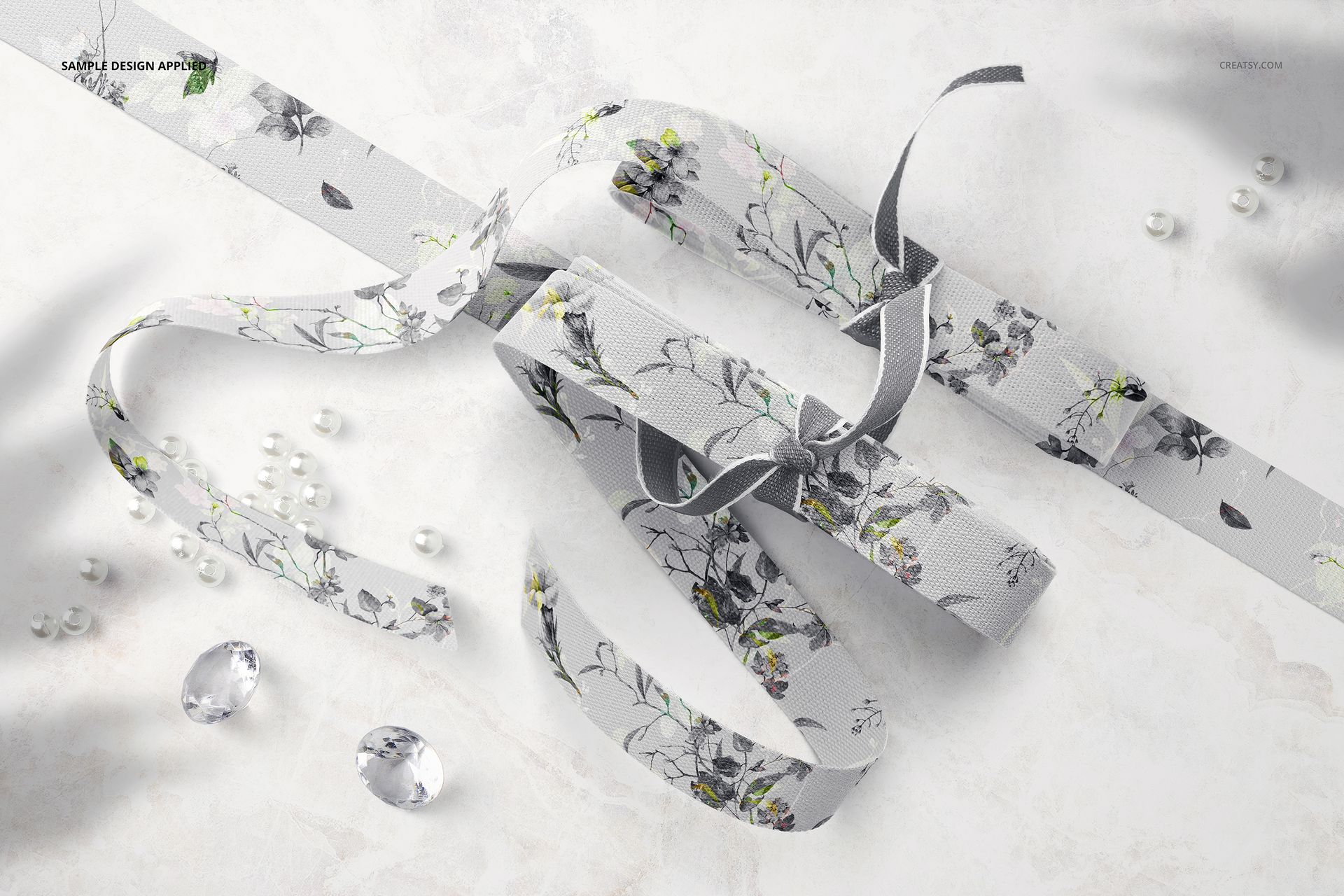Top view of two cotton ribbons with floral patterns and scattered beads on a light marble surface mockup scene.