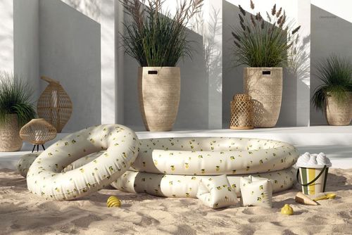 PSD mockup of a round inflatable children's pool in white with yellow accents, surrounded by sand and decorative props.