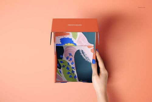 Open mailer box mockup with orange top and vibrant patterned interior, displayed on a solid peach surface.