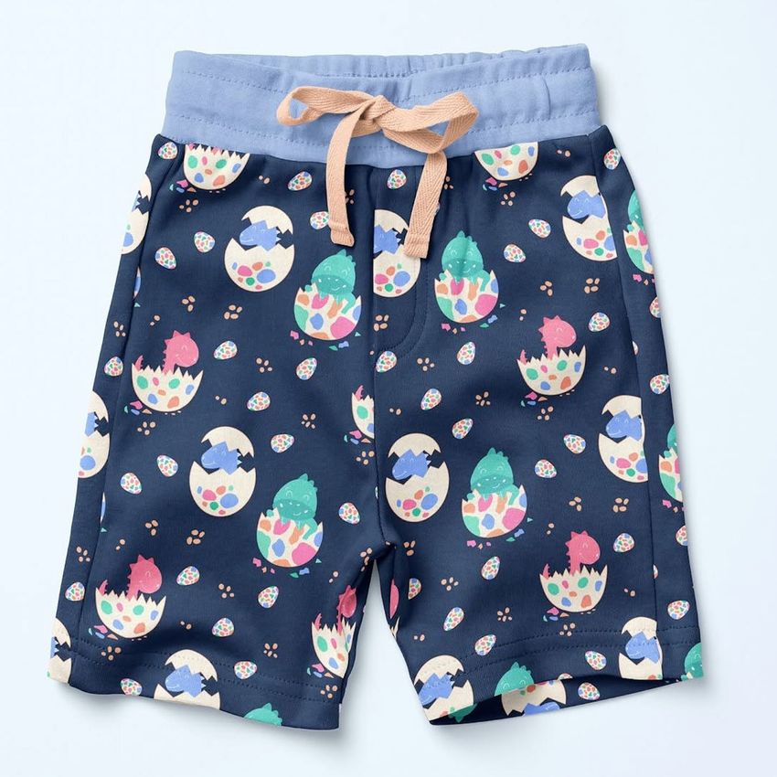 Kids fleece shorts mockup featuring a playful dinosaur and egg pattern in pastel colors on a navy blue background.